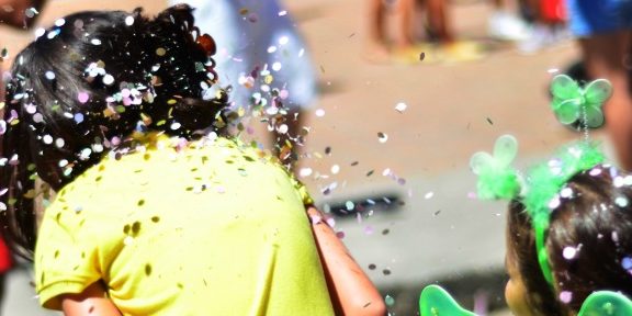 Foto de duas crianças de costas, brincando com confetes.
