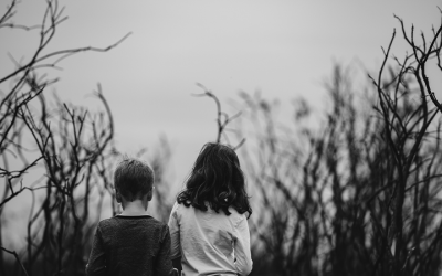 Foto em preto e branco de duas crianças de costas, rodeadas por árvores secas