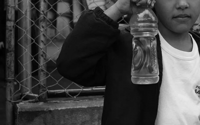 Foto em preto e branco de criança segurando uma garrafa d'água