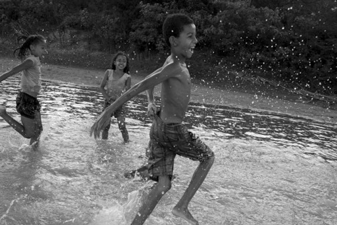 Foto em preto e branco de três crianças brincando no rio