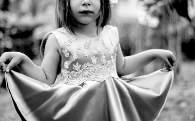 Foto preto e branca de uma menina se cumprimentando com seu vestido.
