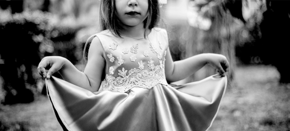 Foto preto e branca de uma menina se cumprimentando com seu vestido.