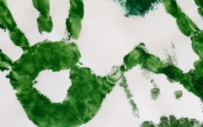 Imagem de mãos pintadas de verde sob um papel branco.