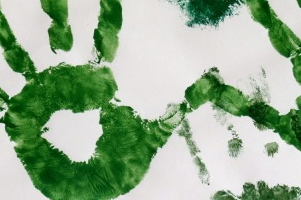 Imagem de mãos pintadas de verde sob um papel branco.
