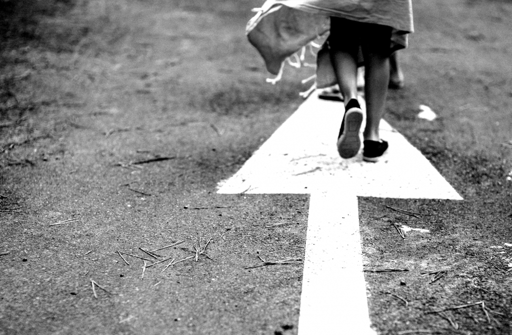 Foto em preto e branco de pés de criança andando sobre seta pintada no chão.