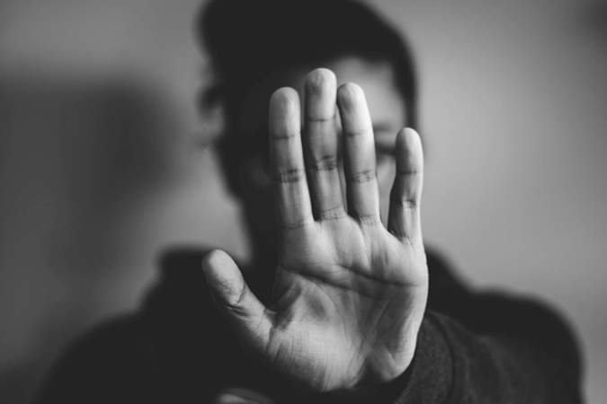 Foto em preto e branco de jovem com a mão frente ao rosto em sinal de pare