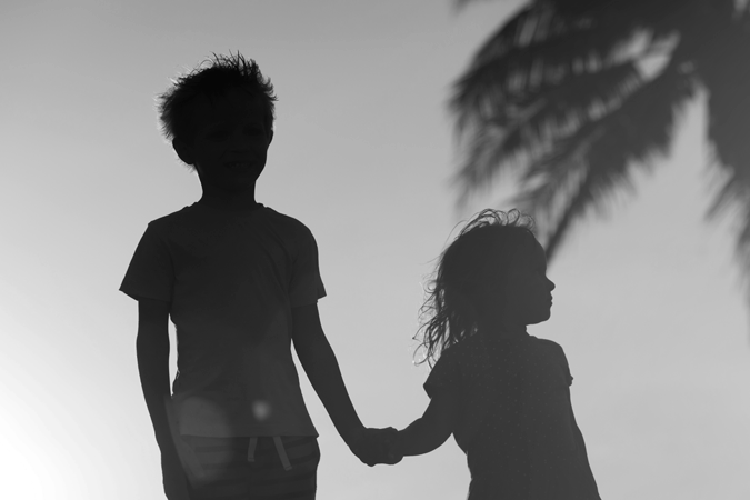 Foto em preto e branco, contraluz, de duas crianças de mãos dadas