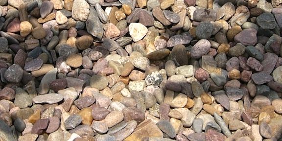 Imagem da sobra de duas mão refletidas em um chão de inúmeras pedras.