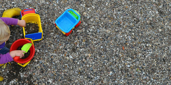 Jesper-Dyhre-Nielsen2-940×347 Imagem de uma vista superior de uma criança brincando ao chão com uma pá e um balde de plástico.