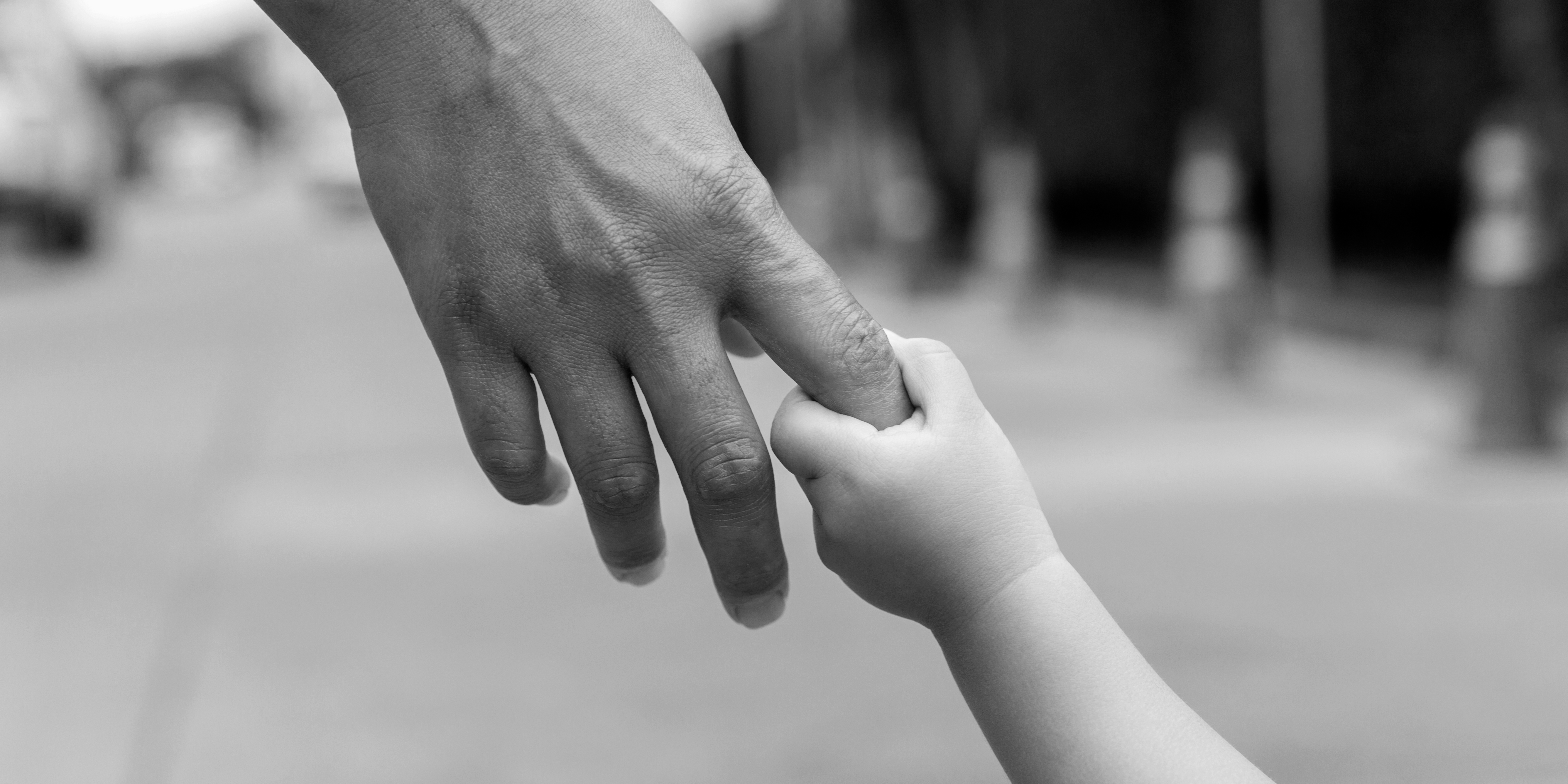 Foto em preto e branco de adulto segurando mão de criança