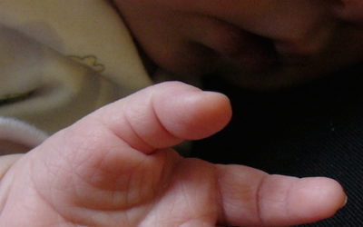 Imagem das mãos e o rosto de um bebê dormindo.