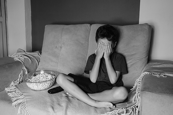 Foto em preto e branco de criança cobrindo os olhos enquanto vê televisão