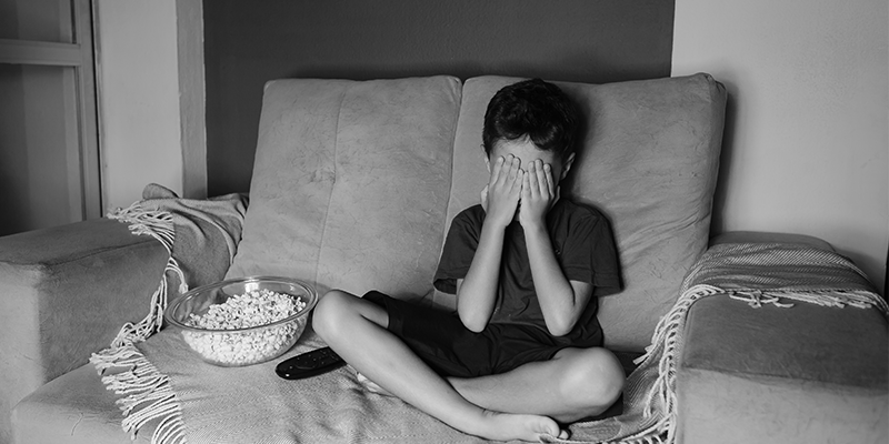 Foto em preto e branco de criança cobrindo os olhos enquanto vê televisão