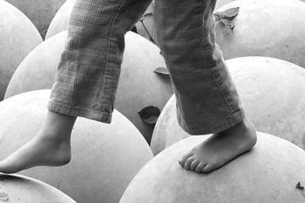 Foto em preto e branco de pés de criança, andando sobre bolas.