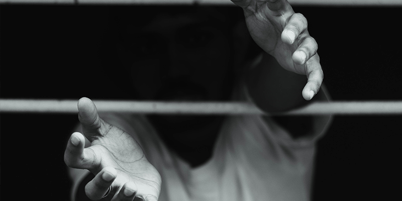 Foto em preto e branco de adolescente com as mãos estendidas para o lado de fora de grades