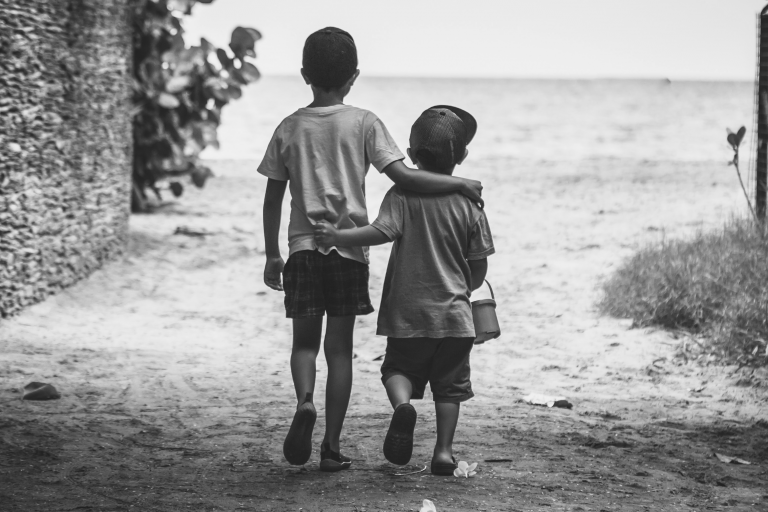 Foto em preto e branco de duas crianças de costas, andando abraçadas