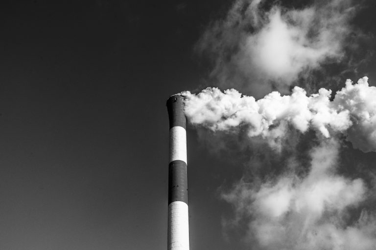 Foto em preto e branco de chaminé de fábrica industrial soltando uma fumaça branca