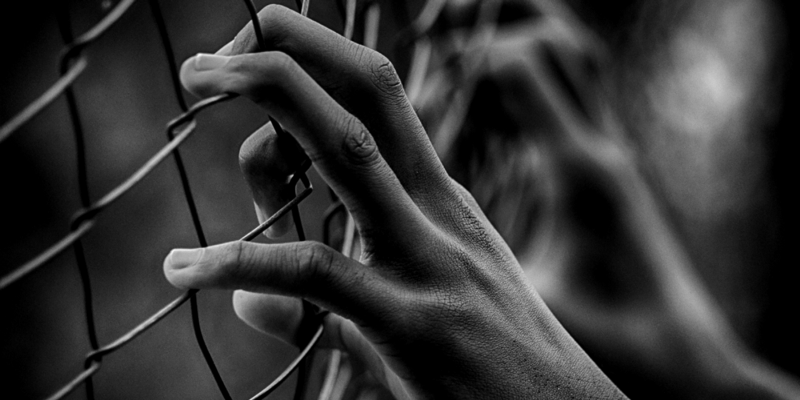 Foto em preto e branco de mãos segurando grades