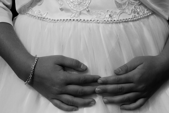 Foto em preto e branco de menina com vestido de noiva e as mãos estendidas sobre o colo