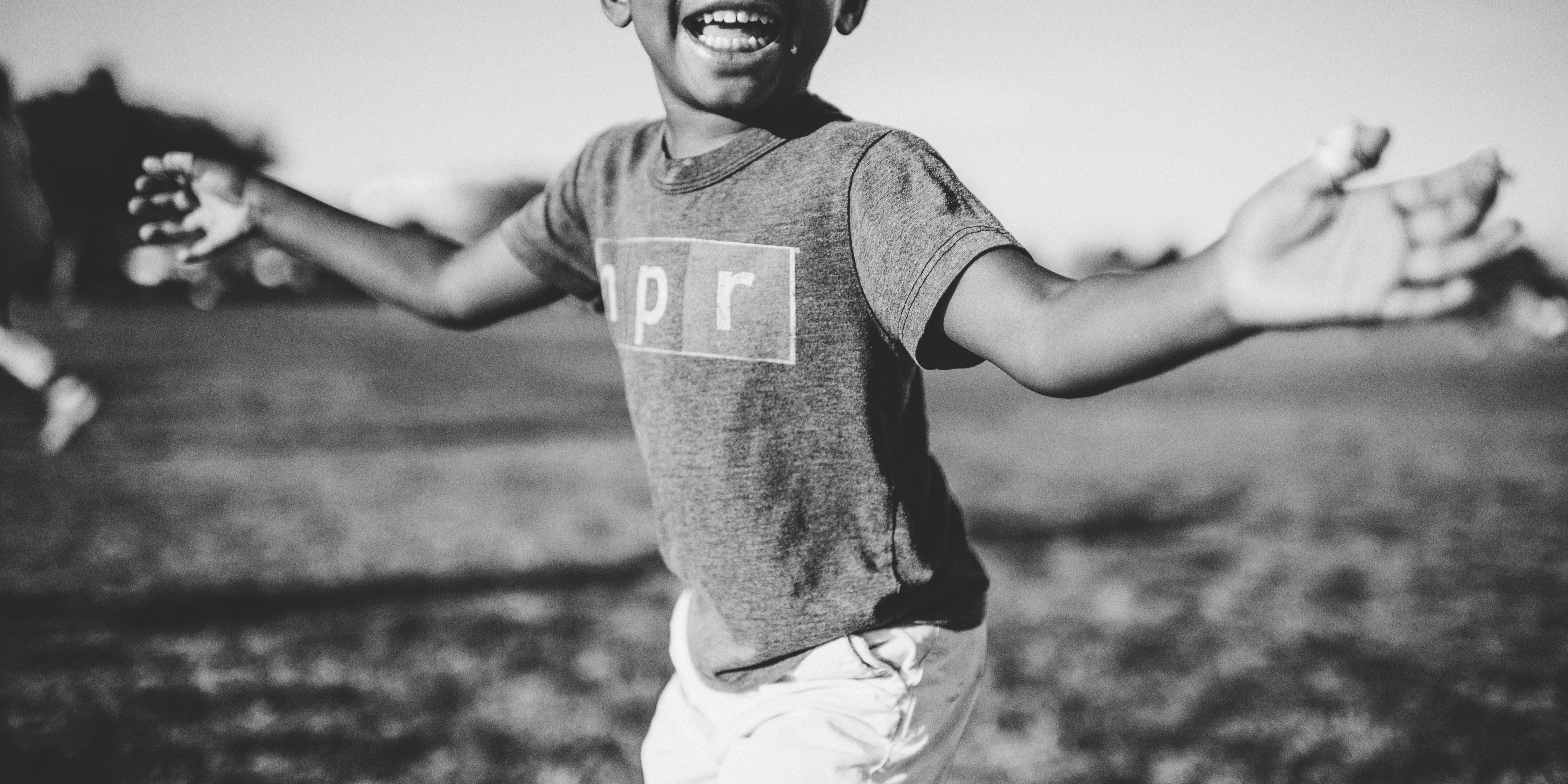 foto em preto e branco de criança sorrindo com os braços abertos