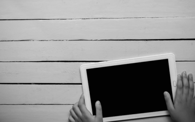 Foto em preto e branca de mão de criança mexendo no tablet - proteção de dados