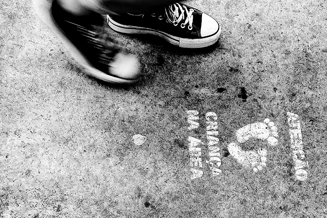 Foto em preto e branco mostra pé de criança próximo a desenho de pés no chão com o texto: atenção, criança na área