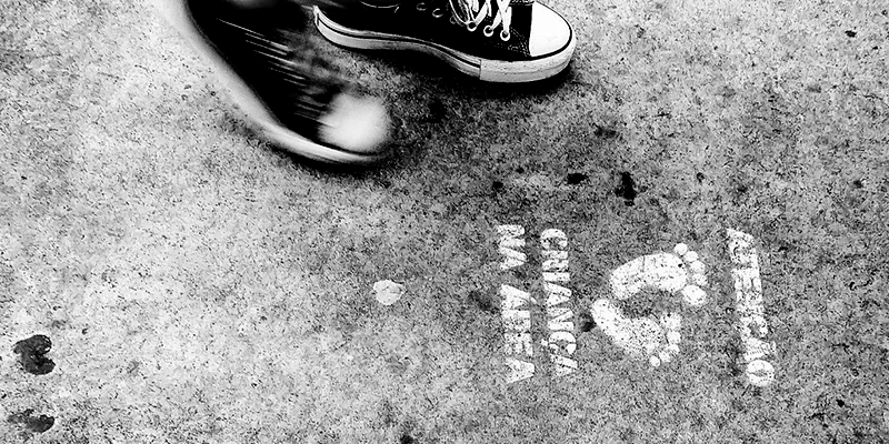 Conanda Foto em preto e branco mostra pé de criança próximo a desenho de pés no chão com o texto: atenção, criança na área