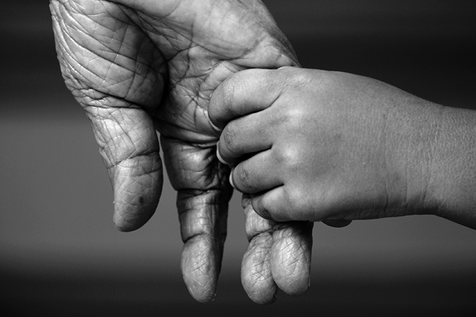 Foto em preto e branco de criança dando a mão para uma pessoa idosa