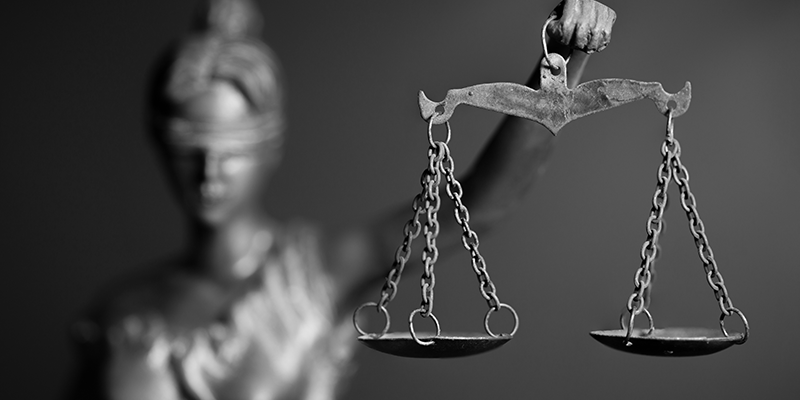 Foto em preto e branco da estátua que representa a Justiça: uma mulher, com os olhos vendados segurando uma balança.