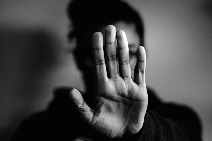 Foto em preto e branco de adolescente com a mão aberta em frente ao rosto como um sinal de "pare"