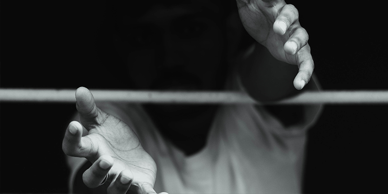 Foto em preto e branco de adolescente com as mãos estendidas para fora de grade