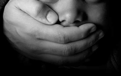 Foto em preto e branco de criança com a boca sendo tampada por um adulto, simbolizando a violência contra crianças durante pandemia