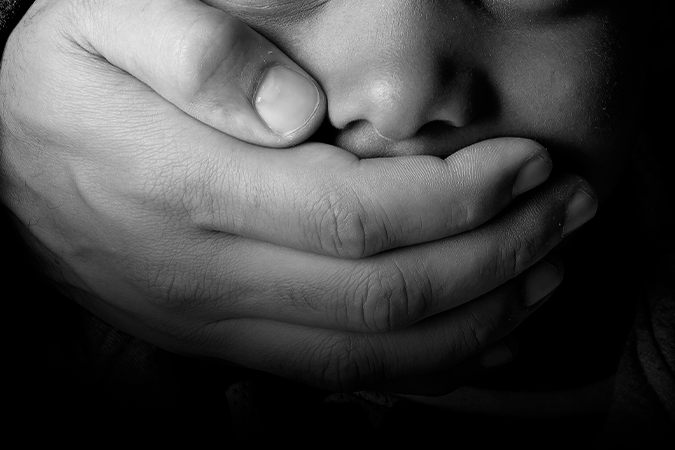 Foto em preto e branco de criança com a boca sendo tampada por um adulto, simbolizando a violência contra crianças durante pandemia