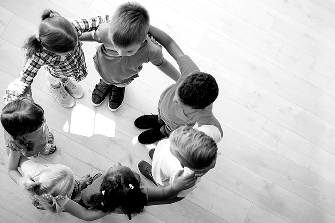 Foto em preto e branco mostra crianças abraçadas em círculo representando união em defesa da primeira infância