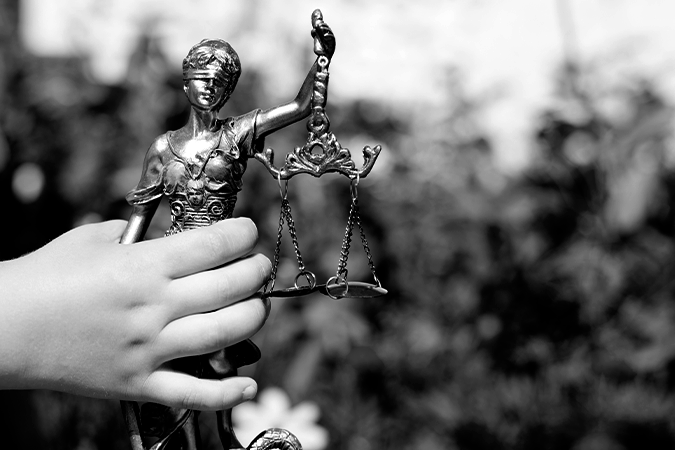 Foto em preto de mão de criança segurando estátua da justiça