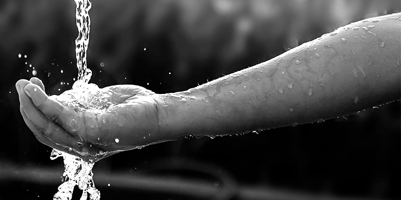 Foto em preto e branco de mão de criança em formato de concha segurando água