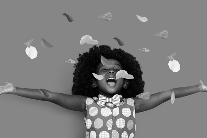 Foto em preto e branco mostra criança com os braços estendidos comemorando enquanto caem confetes