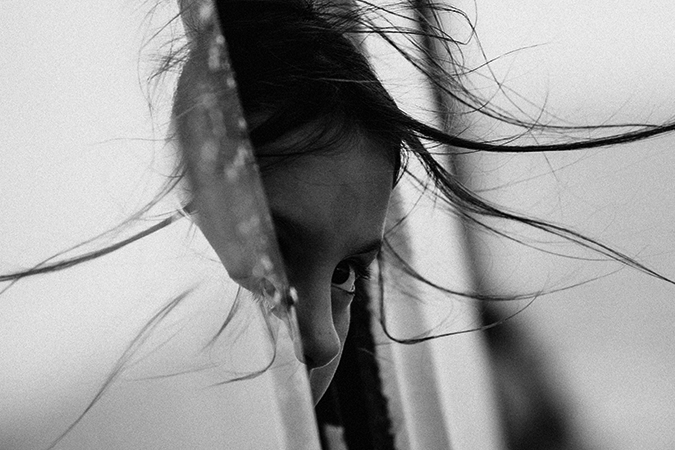 Foto em preto e branco mostra menina com metade do rosto para fora da janela do carro com um olhar assustado