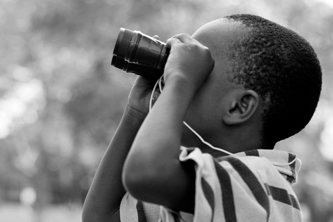 Foto em preto e branco mostra menino com binóculos