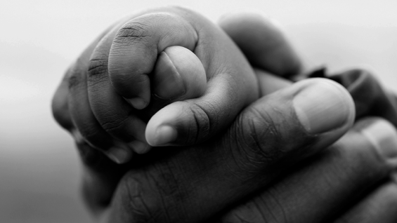 Foto em preto e branco mostra adulto segurando mão de bebê. Representa os impactos do Marco Legal no sistema socioeducativo