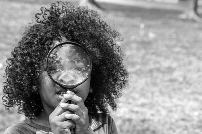Foto em preto e branco mostra criança brincando com lupa, representando o Conanda procurando por organizações para participarem da eleição