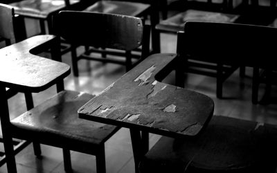 Foto em preto e branco mostra carteiras vazias em sala de aula