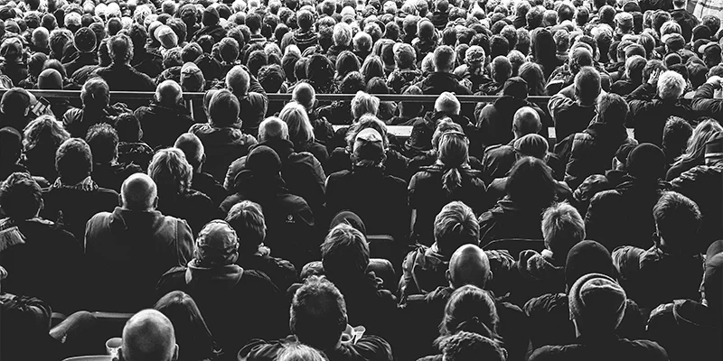 Notícias Foto em preto e branco mostra várias pessoas sentadas em auditório