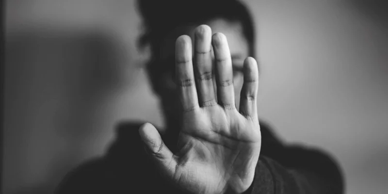 Foto em preto e branco de jovem com a mão frente ao rosto em sinal de pare